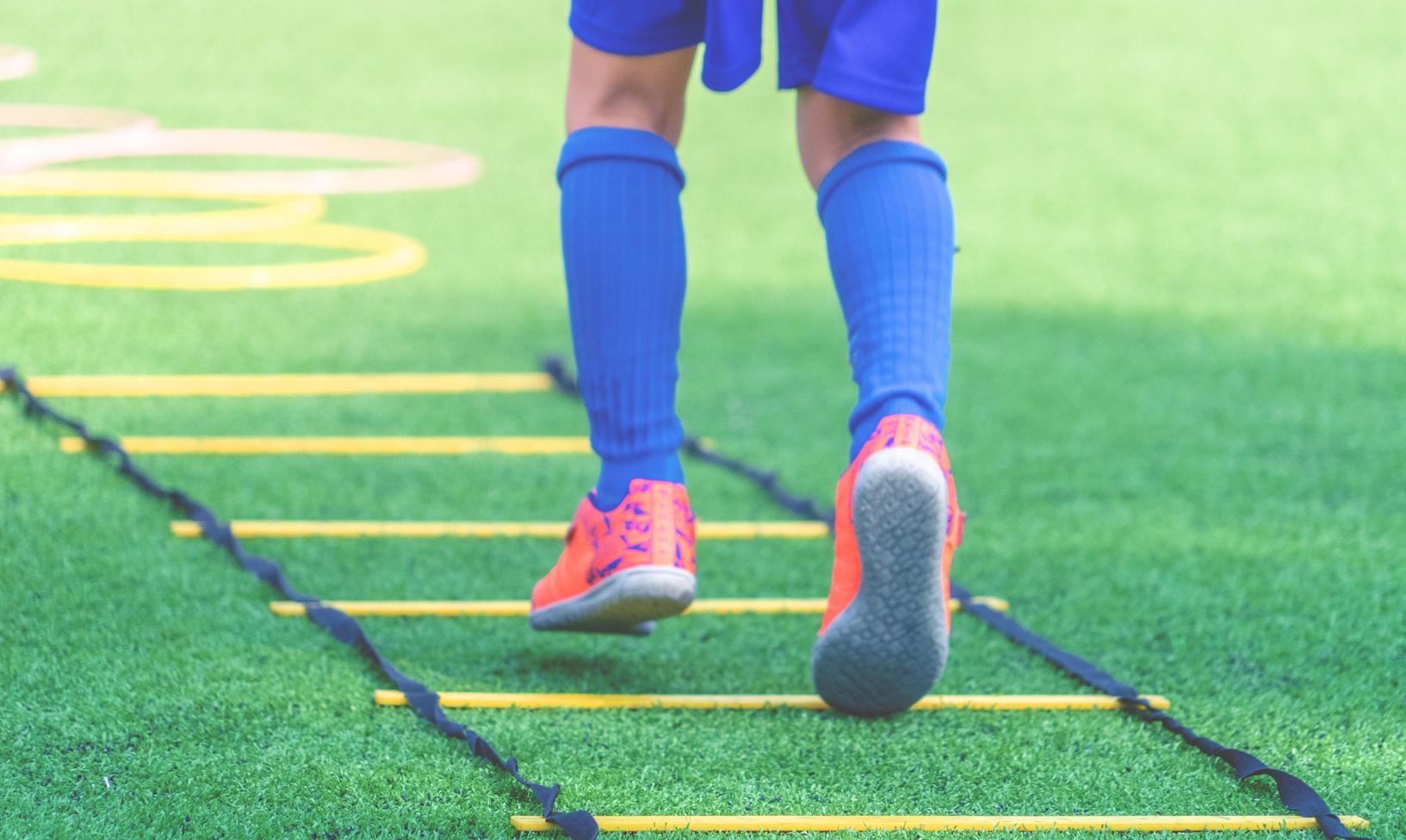 Child feet with soccer boots training on agility speed ladder in soccer training.